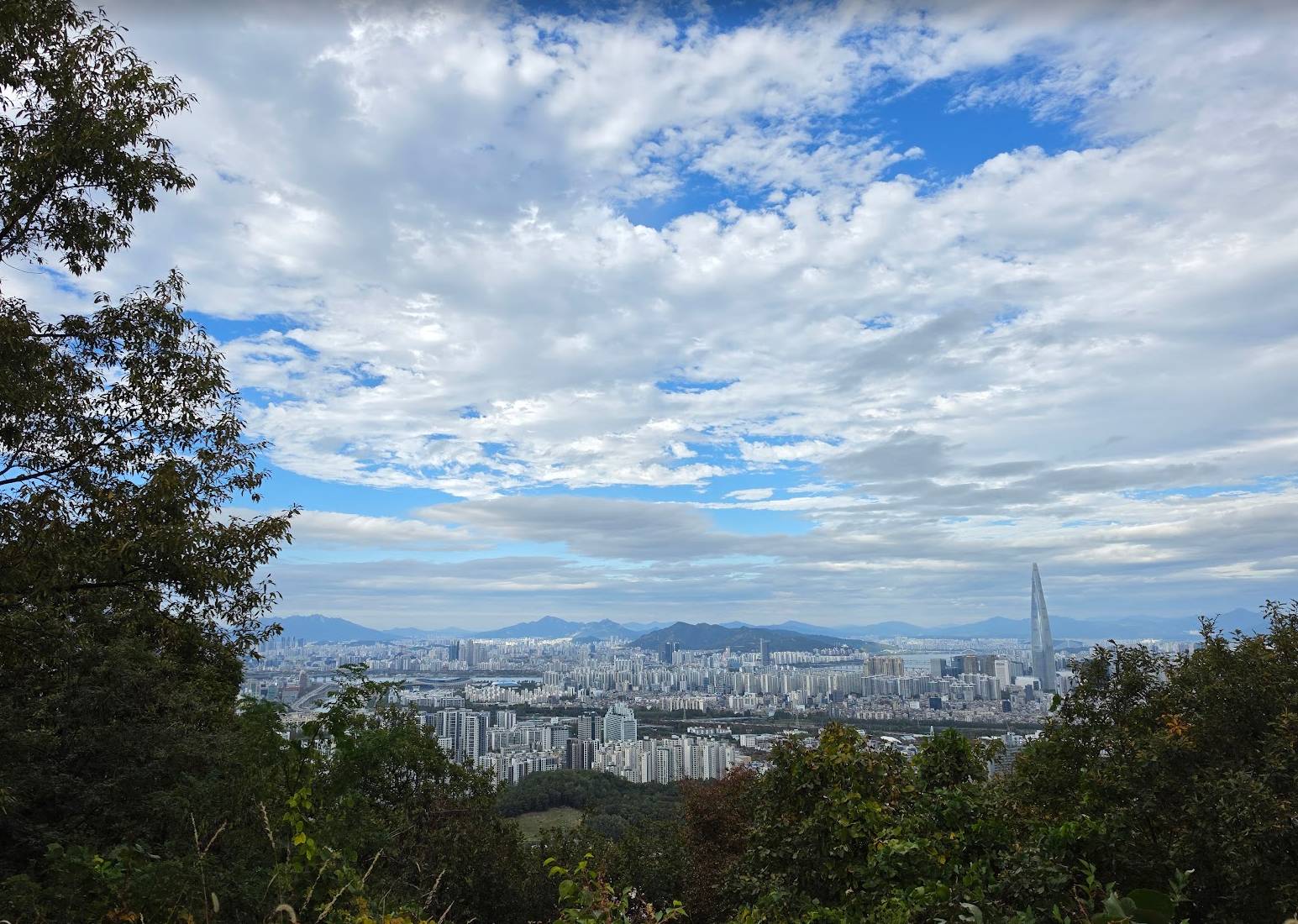 Seoul dilihat dari Guryongsan ke arah pegunungan jauh, Lotte World Tower terlihat
